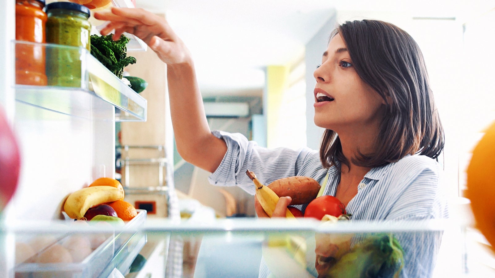Closeup of a cheerful young couple picking some fruit and veggies from the fridge to make some healthy breakfast on Sunday morning. Shot from inside the working fridge.
