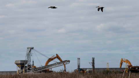 Pelicans fly over construction equipment on Queen Bess Island in Barataria Bay, La., Monday, Feb. 3, 2020. The island provides a crucial nesting ground for pelicans and other seabirds and is being restored to nearly its former size after decades of coastal erosion and the devastating blow of an offshore oil spill 10 years ago. (AP Photo/Gerald Herbert)