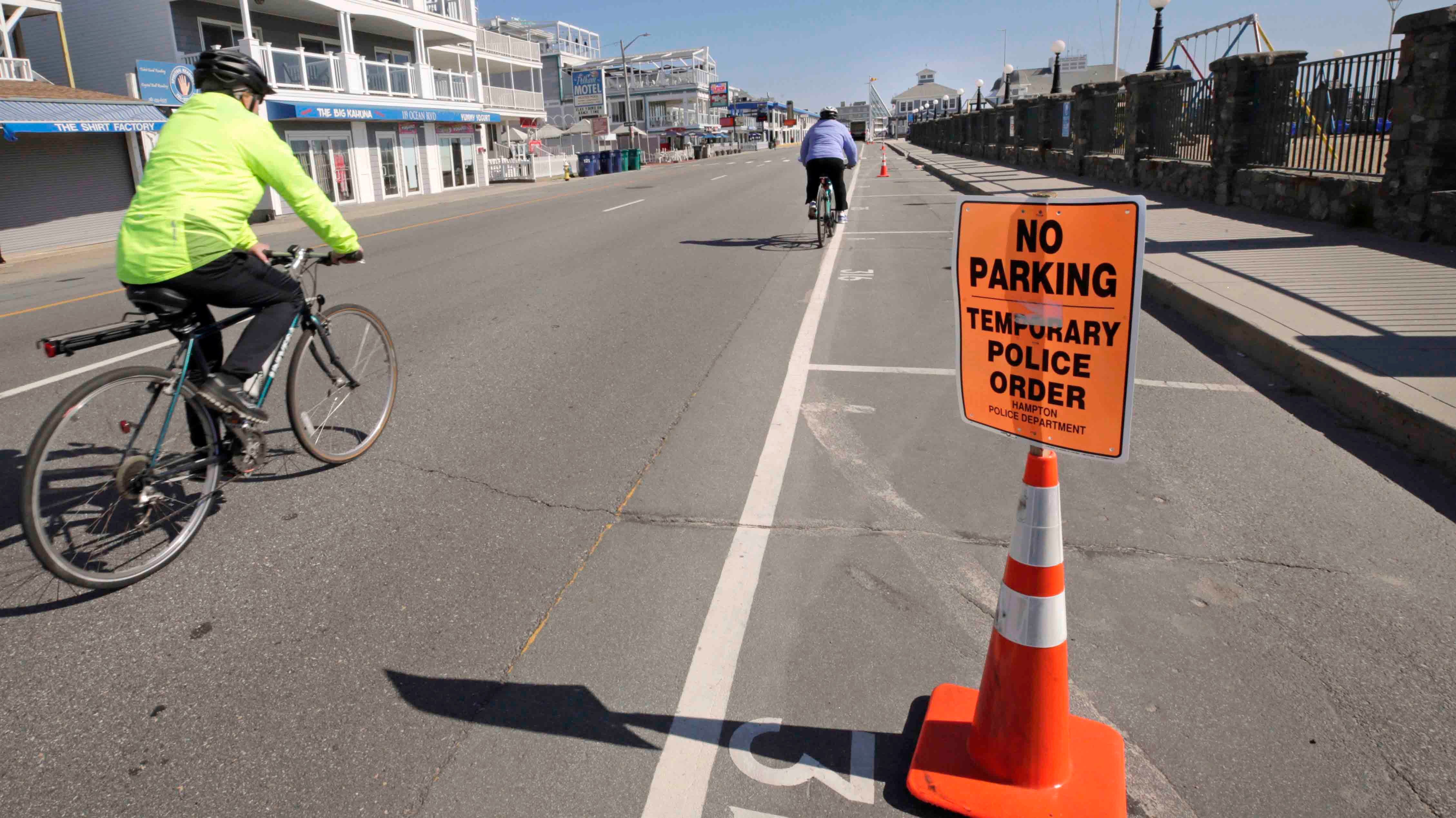 Two cyclists pass empty parking spots adjacent to Hampton Beach in Hampton, N.H., Thursday, May 21, 2020. Beaches in New Hampshire have been closed since March by state order due to the COVID-19 virus outbreak. (AP Photo/Charles Krupa)