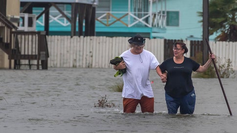 Michael Koudelka and Carol Kelly walk through tidal flood waters on East Hunter Drive in the unincorporated community of Freddiesville near Bayou Vista, Texas on Monday, Sept. 21, 2020. Tidal surge as well as rain showers from the storm continued to inundate low-lying area around Galveston County, Texas. (Stuart Villanueva/The Galveston County Daily News via AP)