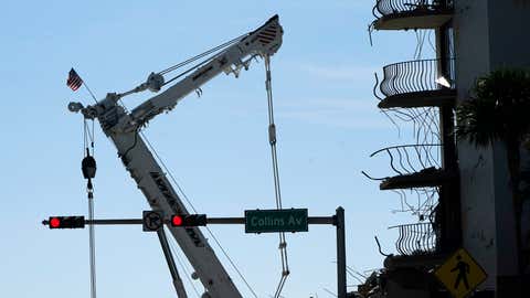 An American flag flies from a crane next to the Champlain Towers South condo building, where scores of victims remain missing more than a week after it partially collapsed, Sunday, July 4, 2021, in Surfside, Fla. Demolition teams were preparing to bring down the unstable remainder of the structure ahead of Tropical Storm Elsa. (AP Photo/Lynne Sladky)
