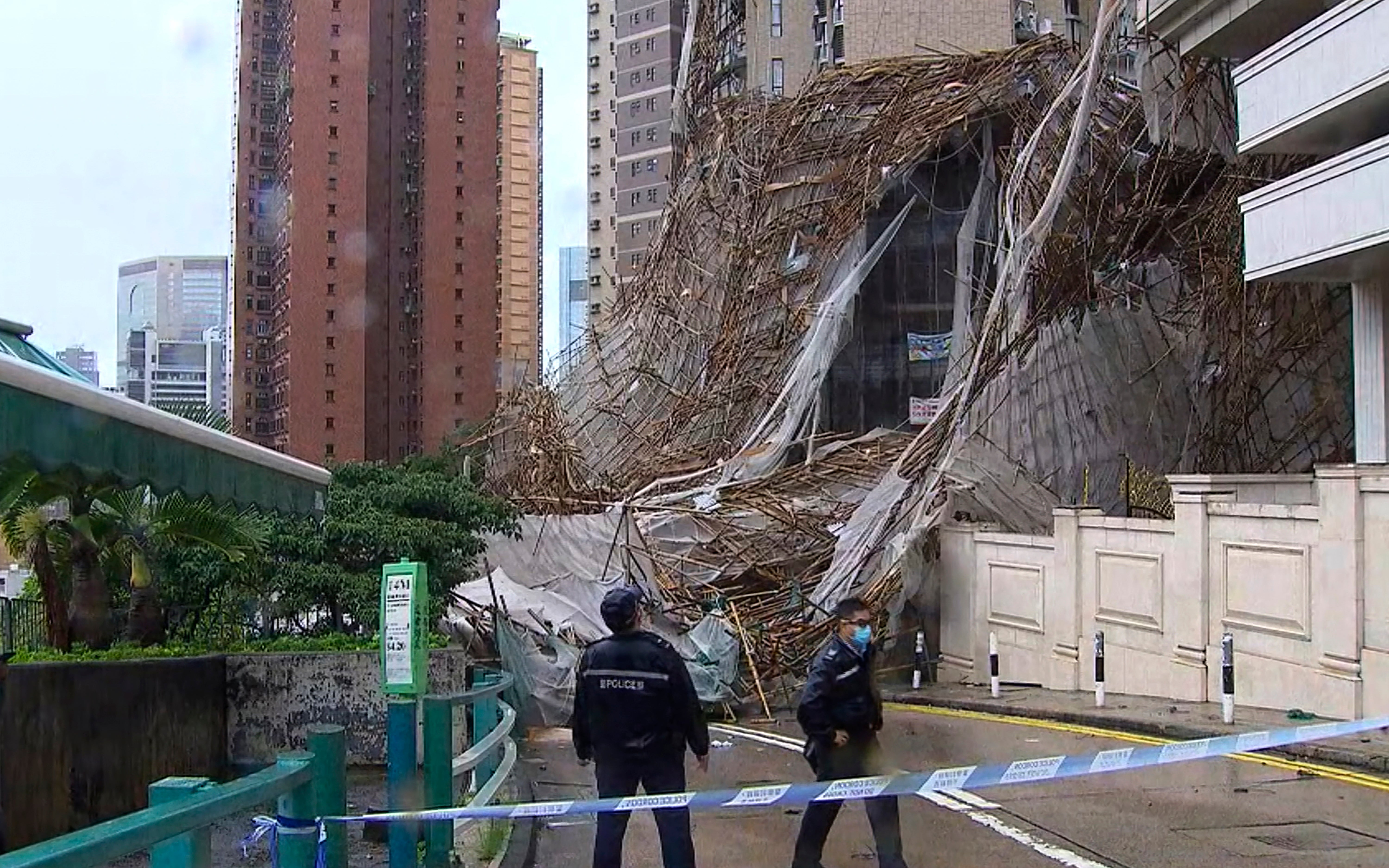 In this image made from video provided by TVB, officials inspect the scene of a section of an apartment building scaffolding that collapsed during heavy weather in Hong Kong, Friday, Oct. 8, 2021. The official Hong Kong Observatory issued a Black Rainstorm Signal Friday, which indicates rainfall of more than 2.76 inches per hour all over the territory, and instructed people to "stay indoors or take shelter in a safe place." (TVB via AP Video)