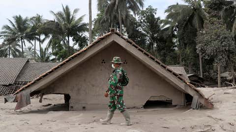 Un soldat indonésien passe devant une maison ensevelie sous les cendres suite à l'éruption du mont Semeru dans le district de Lumajang, province de Java oriental, Indonésie, le dimanche 5 décembre 2021. (AP Photo/Trisnadi)