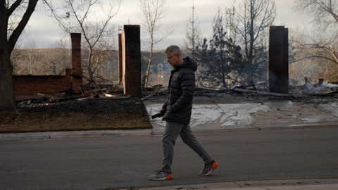 Dan Bruder walks past burned homes in his neighborhood, Dec. 31, 2021, in Superior, Colo. An estimated 580 homes, a hotel and a shopping center have burned and tens of thousands of people were evacuated in wind-fueled wildfires outside Denver, officials said Thursday evening. (AP Photo/Brittany Peterson)