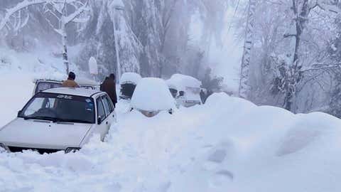 In this photo provided by the Inter Services Public Relations, people walk past vehicles trapped in a heavy snowfall-hit area in Murree, some 28 miles (45 kilometers) north of the capital of Islamabad, Pakistan, Saturday, Jan. 8, 2022. Temperatures fell to minus 8 degrees Celsius (17.6 Fahrenheit) amid heavy snowfall at Pakistan's mountain resort town of Murree overnight, killing multiple people who were stuck in their vehicles, officials said Saturday. (Inter Services Public Relations via AP)