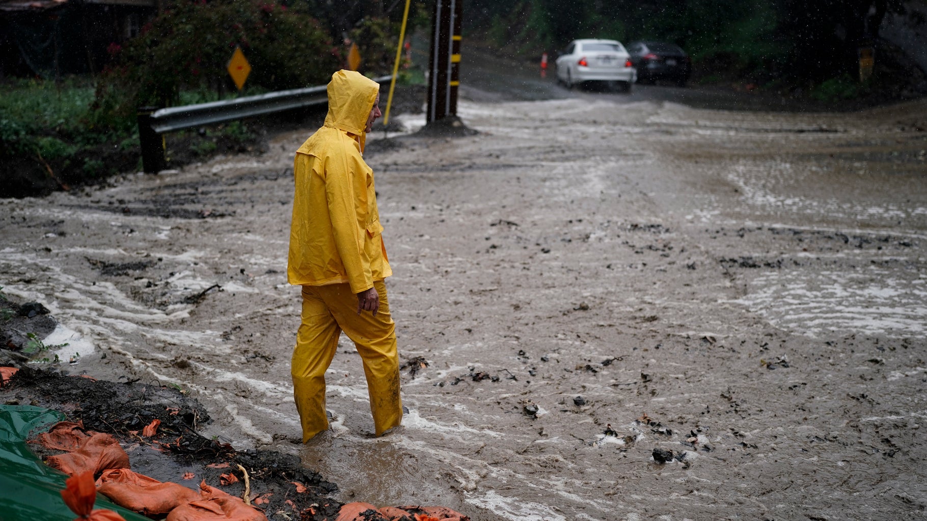 A resident stands on a flooded road during a storm in Silverado Canyon, California, Monday, March 28, 2022. A vigorous late-season storm moved slowly through California on Monday, bringing flood worries as rain fell across wildfire burn scars. (AP Photo/Jae C. Hong)