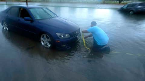 Mon Lun attaches a strap to his stalled car before towing it out of receding floodwaters in Dallas, Monday, Aug. 22, 2022. (AP Photo/LM Otero)