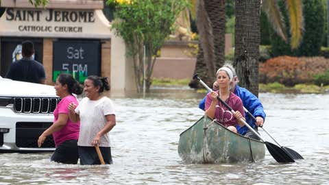 Residents paddle and walk along a flooded road Thursday, April 13, 2023, in Fort Lauderdale, Fla. Over two feet of rain fell causing widespread flooding, closing the Fort Lauderdale airport and turning thoroughfares into rivers. (AP Photo/Marta Lavandier)