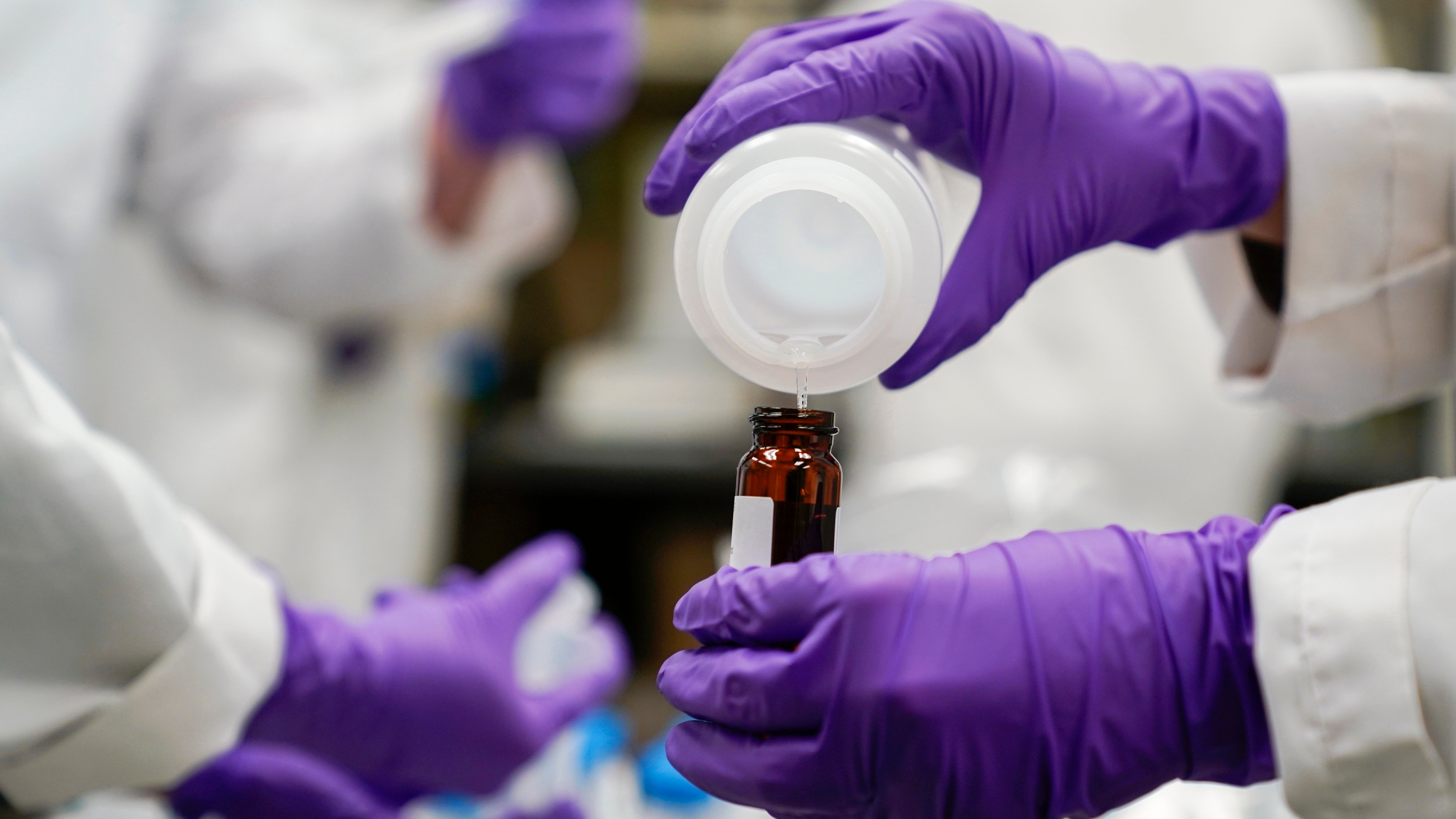 FILE - Eva Stebel, water researcher, pours a water sample into a smaller glass container for experimentation as part of drinking water and PFAS research at the U.S. Environmental Protection Agency Center For Environmental Solutions and Emergency Response on Feb. 16, 2023, in Cincinnati. The 3M chemical company announced Thursday, June, 22, 2023 a $10.3 billion settlement with U.S. water utilities and agencies over PFAS pollution that will allow them to test and treat drinking water contaminated with these &ldquo;forever chemicals.(AP Photo/Joshua A. Bickel, File)