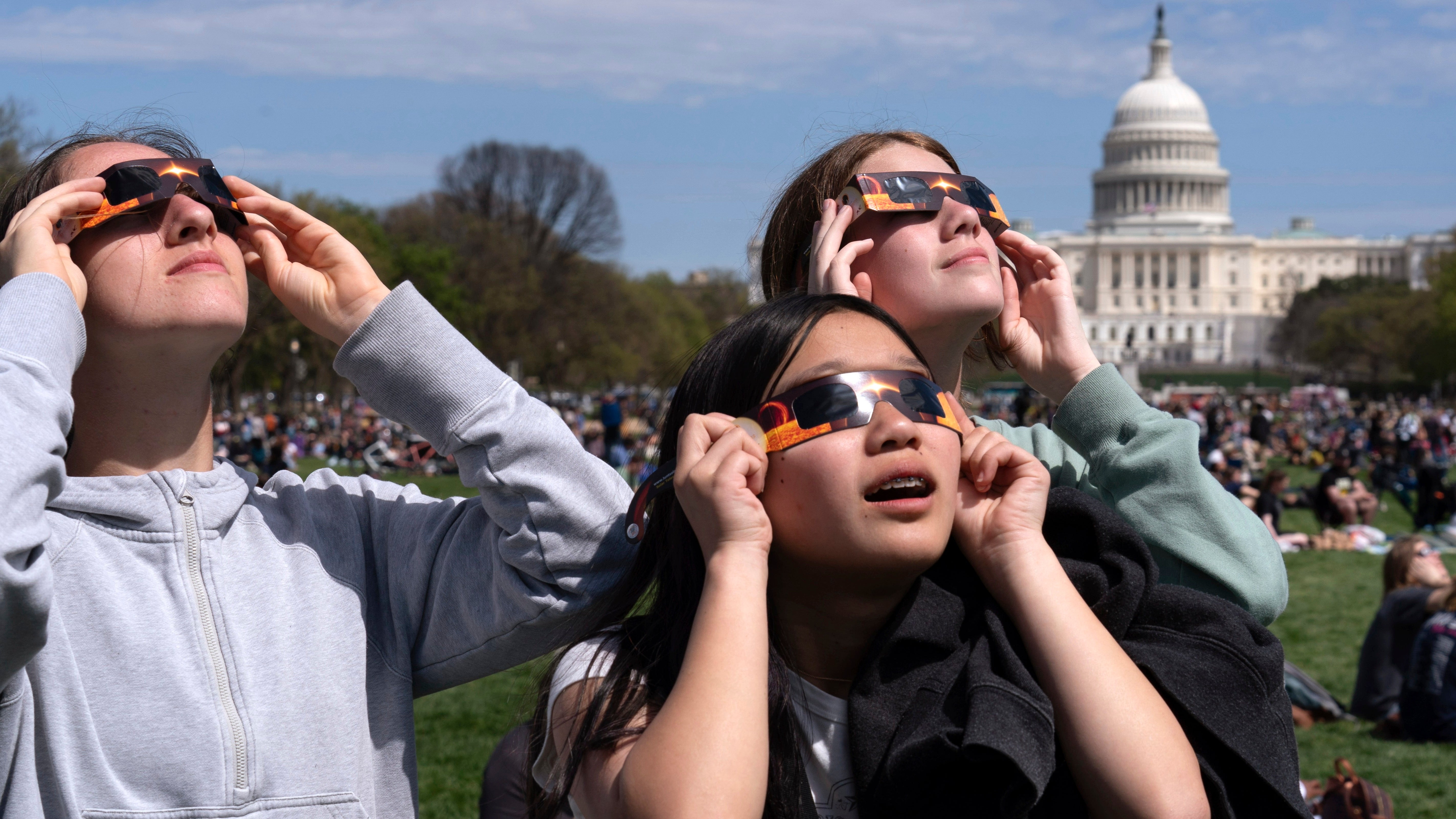 People wear protective glasses as they gather to watch as the moon partially covers the sun during a total solar eclipse, as seen from at National Mall in Washington, Monday, April 8, 2024. (AP Photo/Jose Luis Magana)
