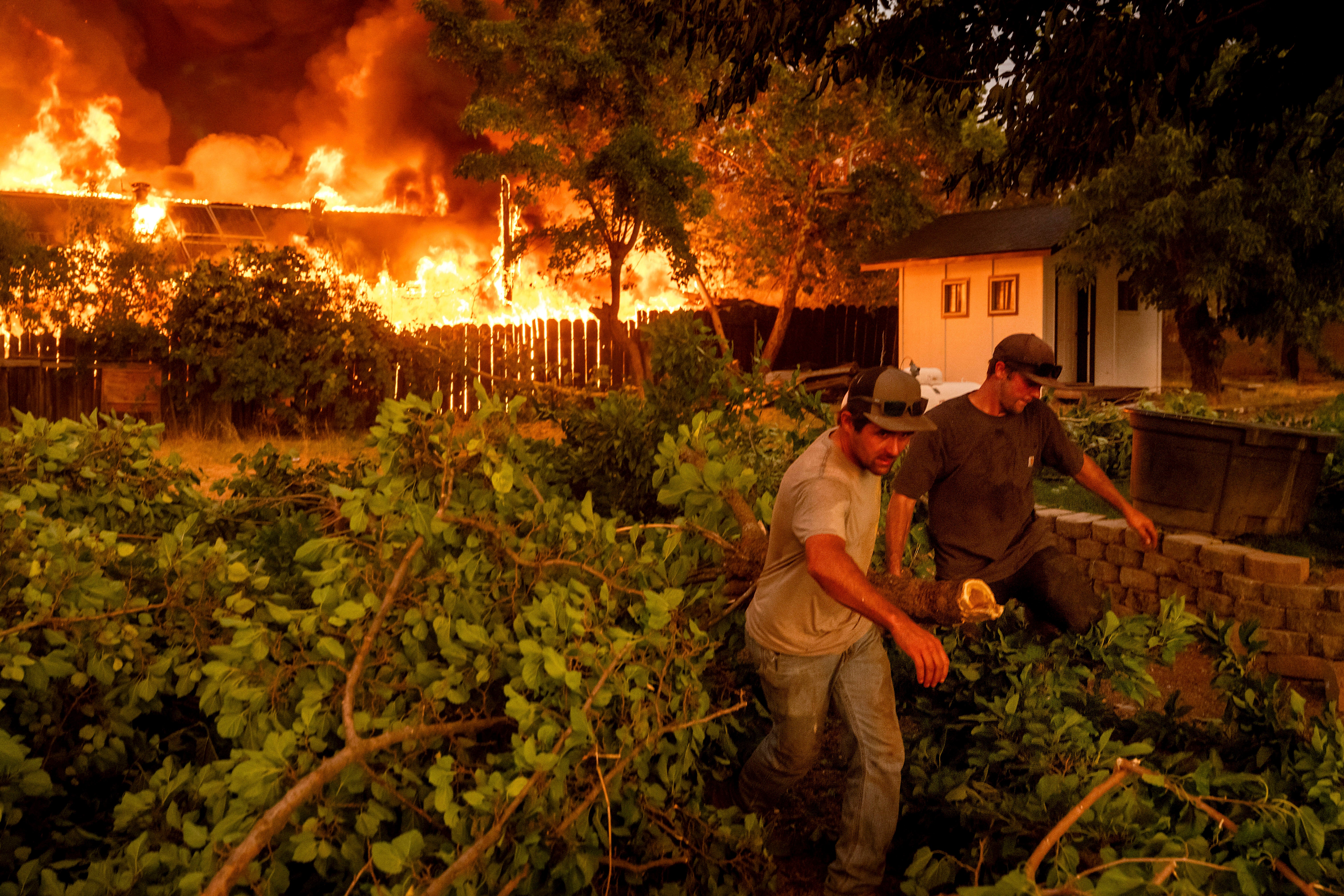 Layne Smith, left, clears vegetation to stop flames from spreading to his home as the 6-5 Fire burns through the Chinese Camp community of Tuolumne County, Calif., on Tuesday, Sept. 2, 2025. (AP Photo/Noah Berger)