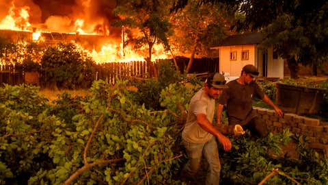 Layne Smith, left, clears vegetation to stop flames from spreading to his home as the 6-5 Fire burns through the Chinese Camp community of Tuolumne County, Calif., on Tuesday, Sept. 2, 2025. (AP Photo/Noah Berger)
