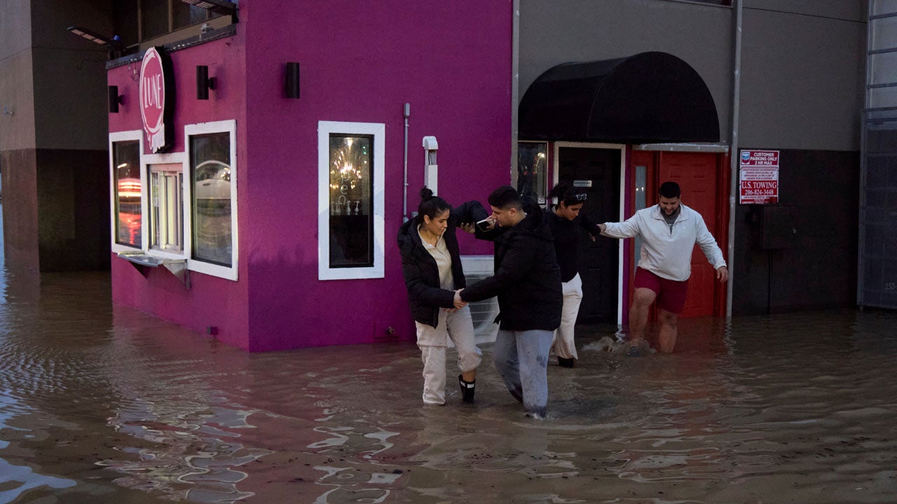 Owners of a deli business, Zahrha Hesham, left, and her brother Karrar Hesham, right, steady each other with along with Hanadi Hesham, and Yousif Hesham, behind, as they walk through the floodwaters after checking on the state of the store, Wednesday, Dec. 10, 2025, in Auburn, Washington. (AP Photo/John Froschauer)