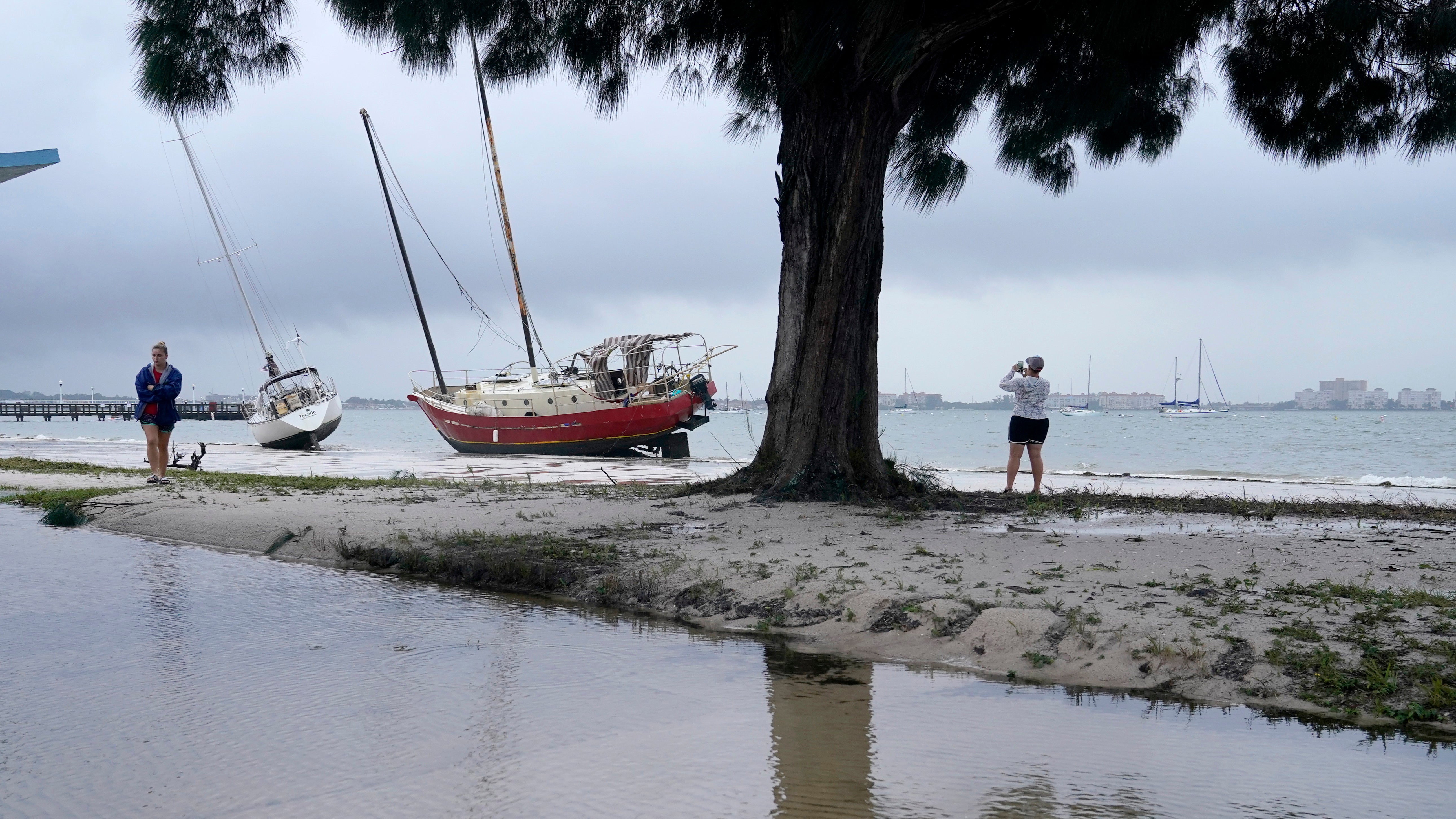 People walk past past boats on the beach in the aftermath of Tropical Storm Eta, Thursday, Nov. 12, 2020, in Gulfport, Fla. Eta dumped torrents of blustery rain on Florida's west coast as it slogged over the state before making landfall near Cedar Key, Fla. (AP Photo/Lynne Sladky)