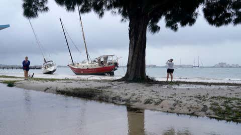 People walk past past boats on the beach in the aftermath of Tropical Storm Eta, Thursday, Nov. 12, 2020, in Gulfport, Fla. Eta dumped torrents of blustery rain on Florida's west coast as it slogged over the state before making landfall near Cedar Key, Fla. (AP Photo/Lynne Sladky)