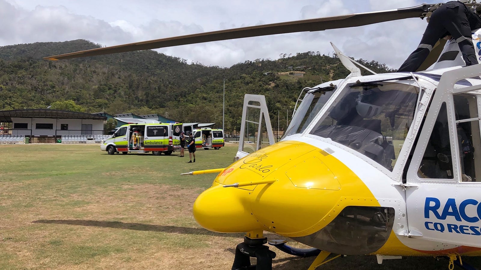 In this photo provided by Royal Automobile Club of Queensland (RACQ) Rescue, a helicopter and ambulances used in the rescue of two tourists attacked by a shark are parked on a sporting ground, near Airlie Beach, Australia. A shark bit off a British tourist's foot and mauled another British tourist's leg as the men snorkeled on Australia's Great Barrier Reef, officials said. (RACQ via AP)