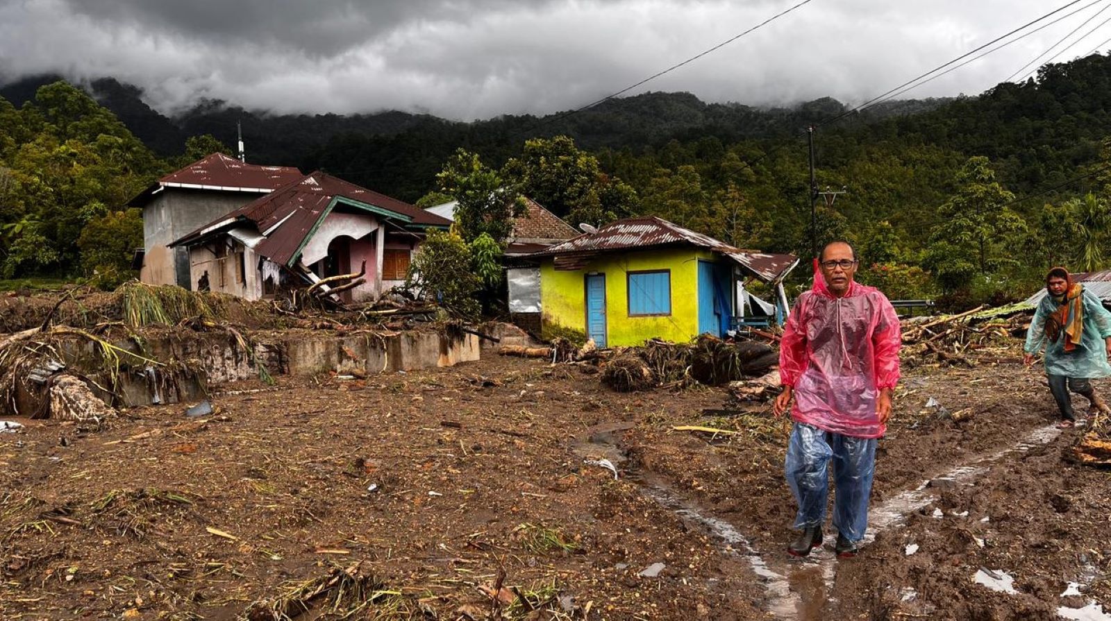 People walk past damaged houses at a village affected by flood in Malalak, West Sumatra, Indonesia, Friday, Nov. 28, 2025. (AP Photo/Ade Yuandha)