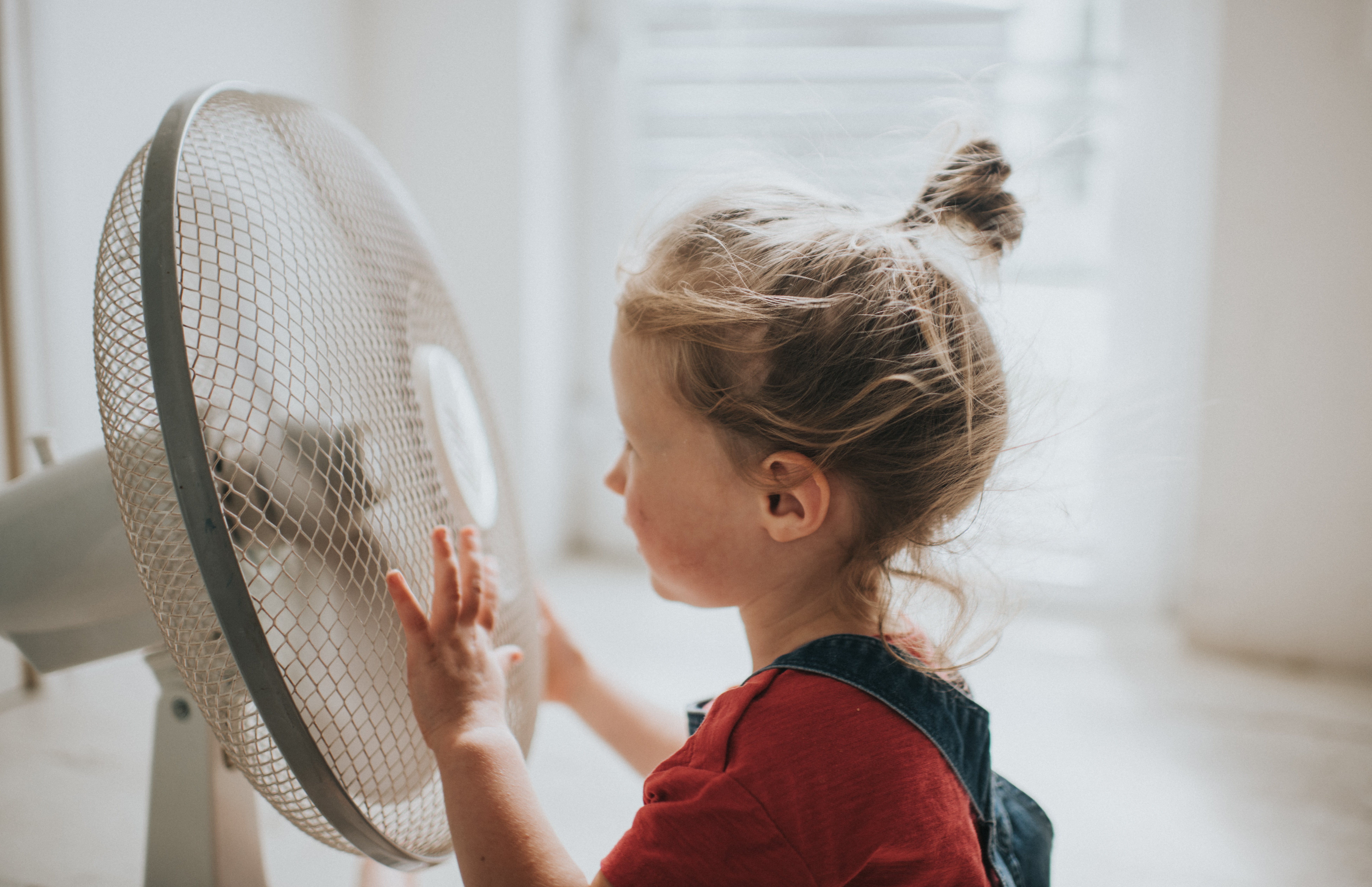 Little girl enjoying cooling experience of sitting by a large electric fan.