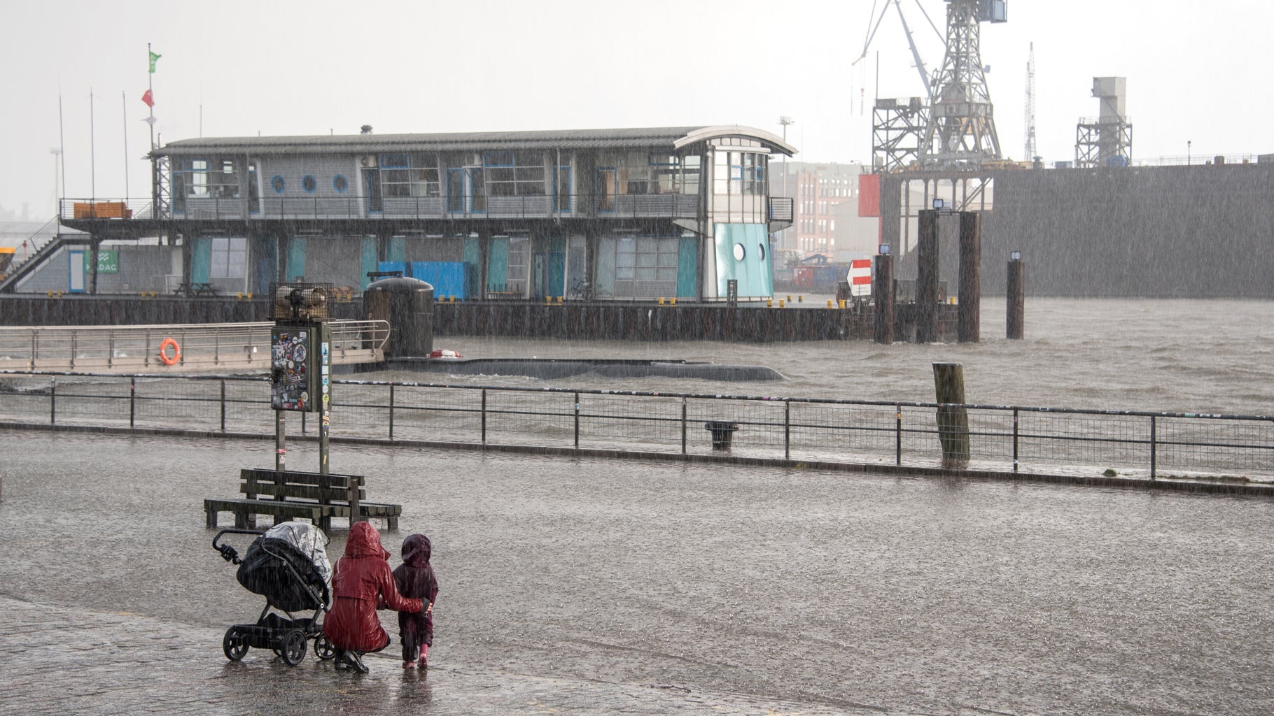 A woman and a child stand at the flooded fish market amid the high water of the Elbe River, Thursday, Feb. 17, 2022, in Hamburg, Germany. (Photo by Daniel Bockwoldt/picture alliance via Getty Images)