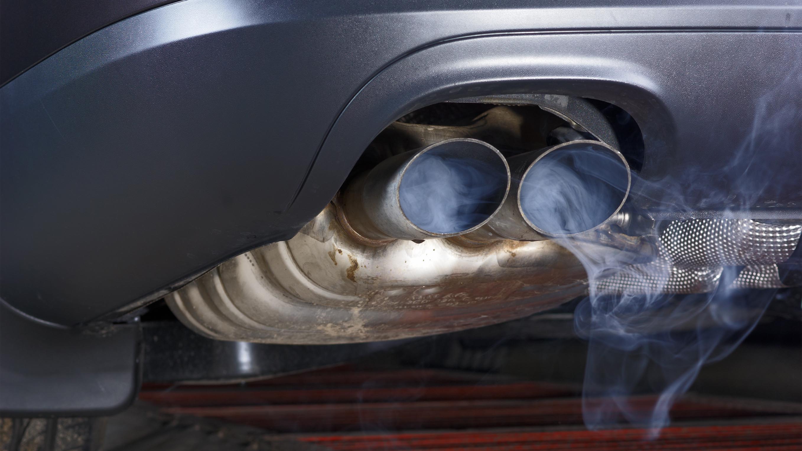 Exhaust pipe of a car - blowing out the pollution. Exhaust pipe coming out of the car with its exhaust. View from below, see the bottom of the exhaust pipe silver. Visible rear bumper eclipse of gray.