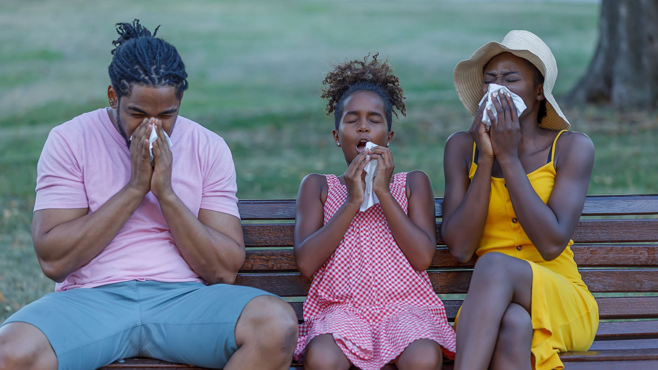 A family is sitting in a public park and blowing their noses in handkerchiefs due to the problems with cold or flu.