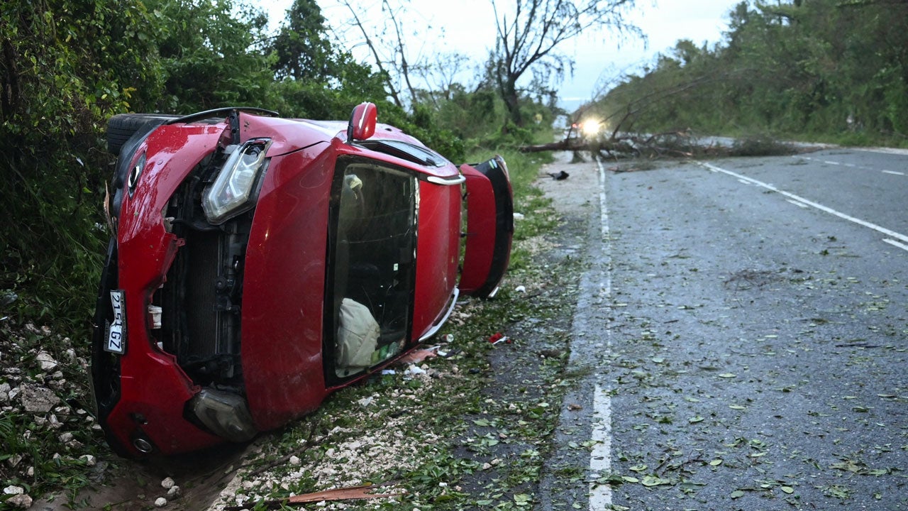 A damaged car by a fallen tree is seen after the passage of Hurricane Melissa in Manchester, Jamaica, on October 28, 2025. (Photo by RICARDO MAKYN/AFP via Getty Images)
