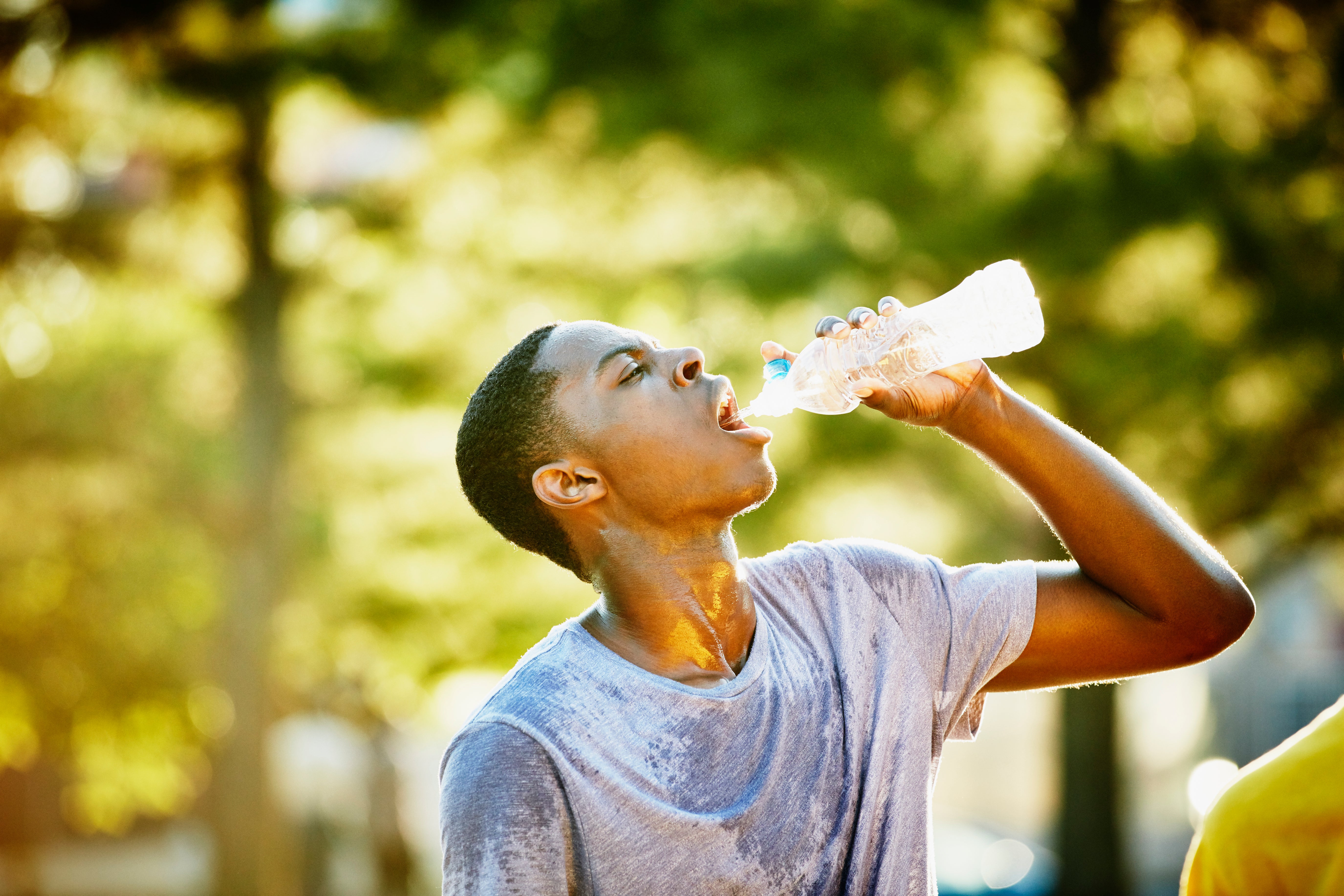 Basketball player drinking water during break in pickup game with friends on outdoor basketball court