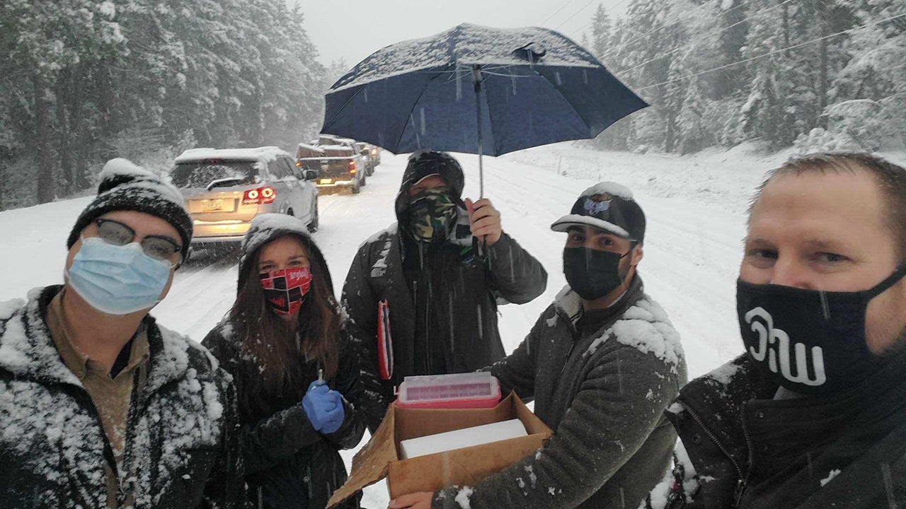 Members of a team from Josephine County Public Health stand in a snowstorm on U.S. Highway 199 near Grants Pass, Oregon, on Tuesday, January 26, 2021. The health department team had six doses of COVID-19 vaccine that would have expired while they were stuck on the highway after it shut down because of an accident during a snowstorm. (Facebook/Josephine County Public Health)