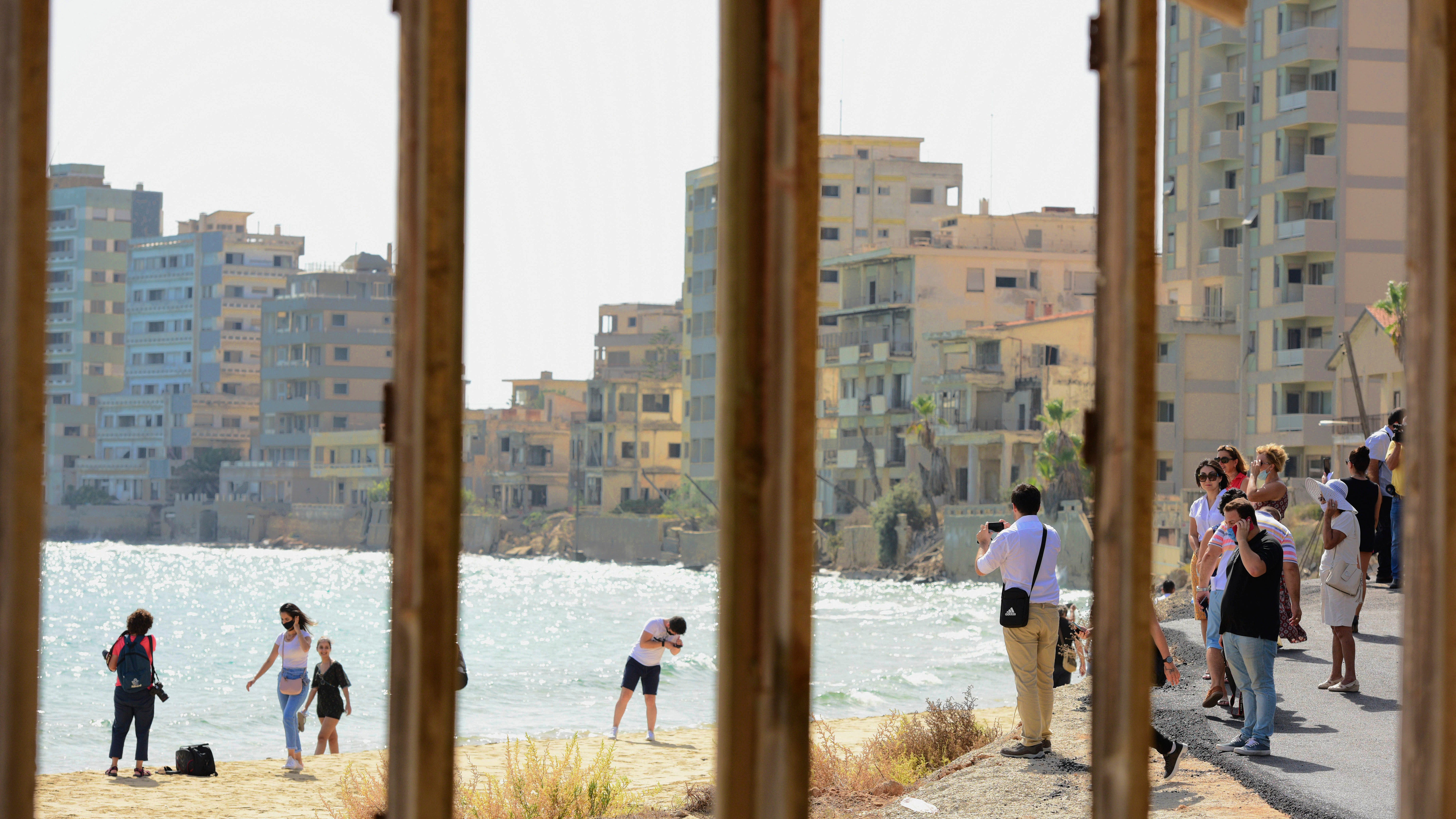 Varosha: Menschen fotografieren eine Strandpromenade neben verlassenen Hotels (Blick durch einen Fensterrahmen).