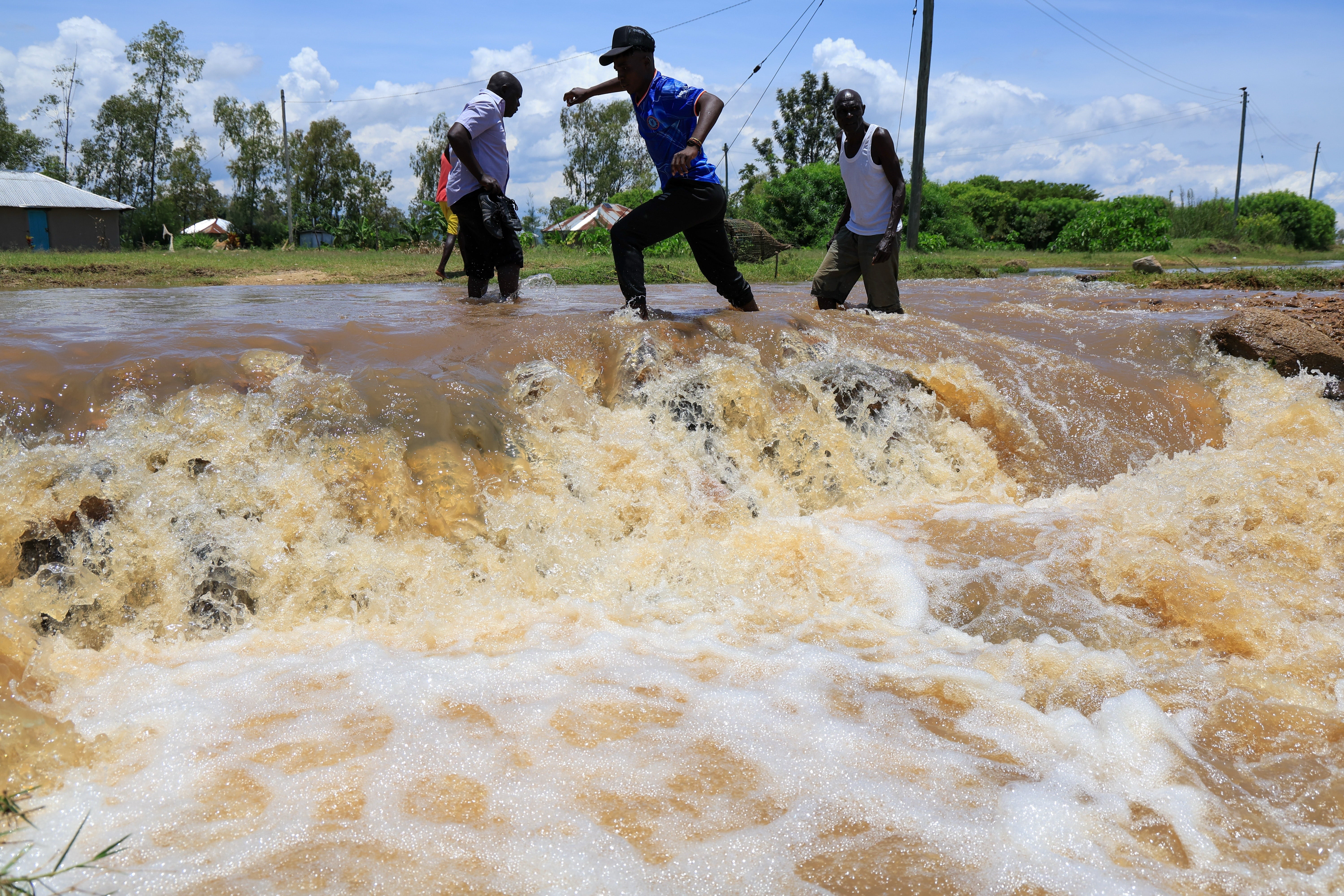 24.03.2026, Kenia, Ahero: Menschen &uuml;berqueren einen &uuml;berfluteten Stra&szlig;enabschnitt nach schweren Regenf&auml;llen. Foto: Andrew Kasuku/AP/dpa +++ dpa-Bildfunk +++