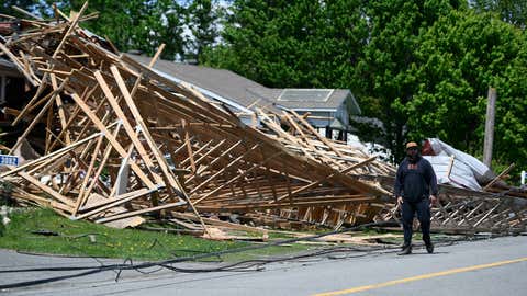 A person walks past a part of the roof of a hardware store that lifted off and crashed into neighboring houses during a major storm, in the community of Hammond in Clarence-Rockland, Ontario, on Monday, May 23, 2022. (Justin Tang/The Canadian Press via AP)