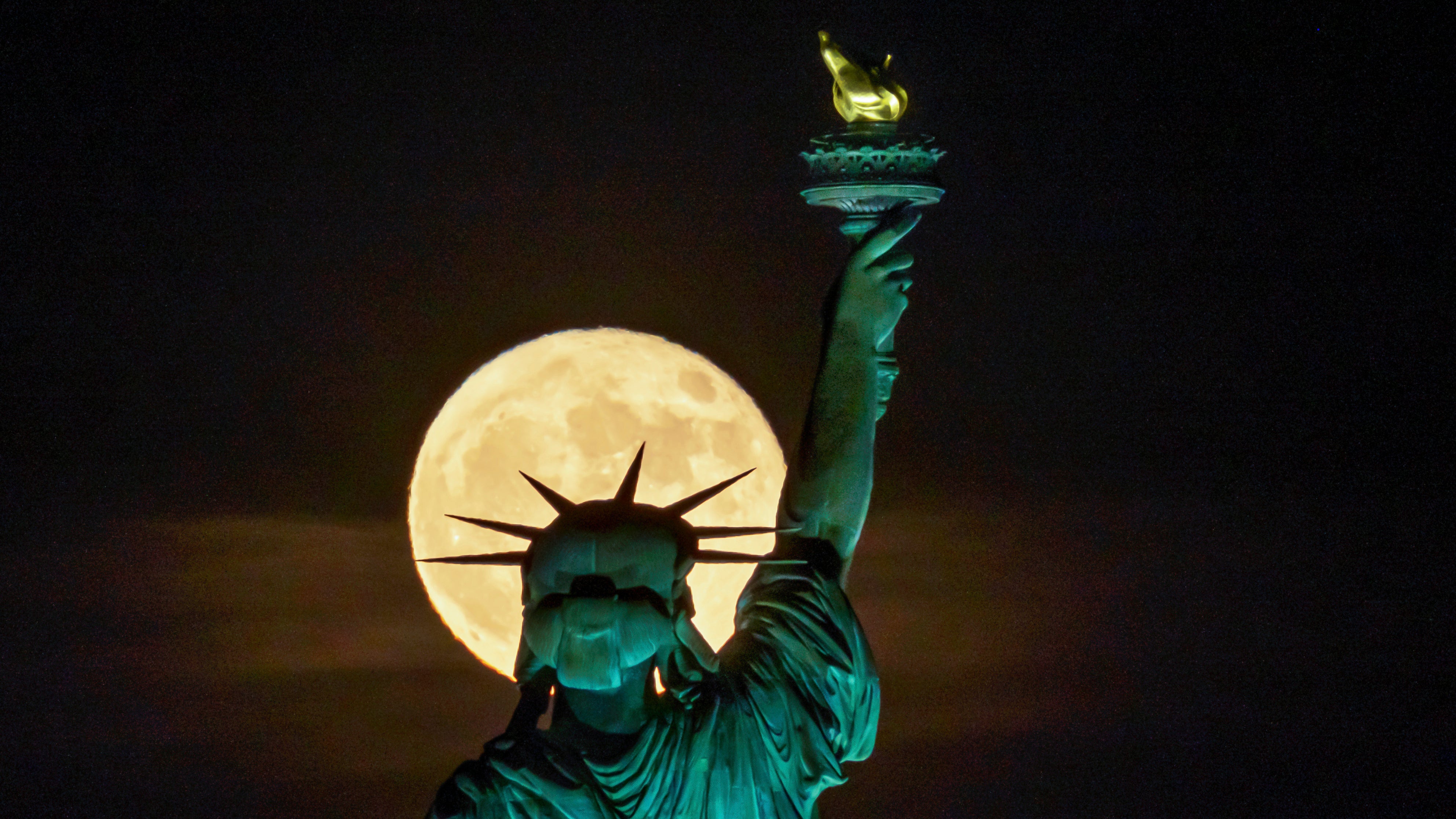 The Strawberry Supermoon rises in front of the Statue of Liberty in New York, late Tuesday, June 14, 2022. (AP Photo/J. David Ake)