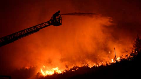 A firefighter standing on a ladder directs high-pressure water from a hose on encroaching flames as crews battled a huge wildfire in the foothills of the Pentadaktylos mountain range in the breakaway north of ethnically divided Cyprus on Thursday, June 23, 2022. Israel on Thursday dispatched two water-dropping aircraft to help in fighting the wildfire that has scorched at least 15 square miles of forest. (AP Photo/Nedim Enginsoy)