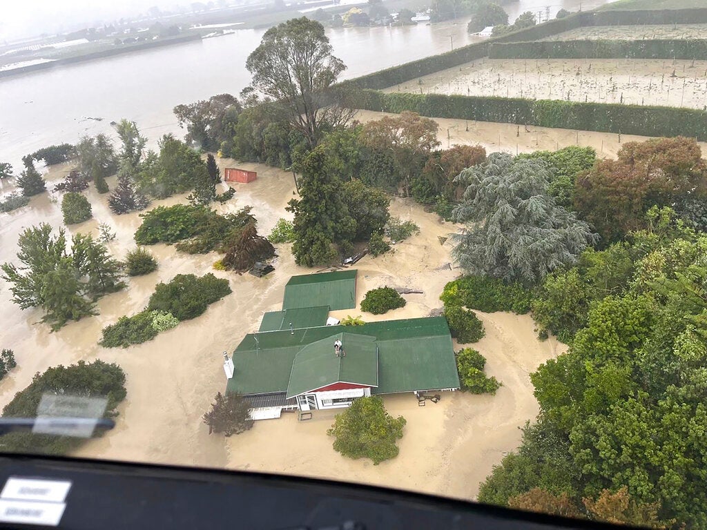 In this image released by the New Zealand Defense Force on Wednesday, Feb. 15, 2023, people stand on a rooftop of a home waiting to be winched to safety by helicopter in the Esk Valley, near Napier, New Zealand. The New Zealand government declared a national state of emergency Tuesday after Cyclone Gabrielle battered the country's north in what officials described as the nation's most severe weather event in years. (New Zealand Defense Force via AP)