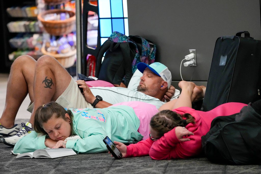 Travelers use their electronic devices while lying on the floor of the departures area of Terminal B at LaGuardia Airport, Tuesday, June 27, 2023, in New York.  Travelers waited out widespread delays at U.S. airports on Tuesday, an ominous sign heading into the long July 4 holiday weekend, which is shaping up as the biggest test yet for airlines that are struggling to keep up with surging numbers of passengers. (AP Photo/Mary Altaffer)