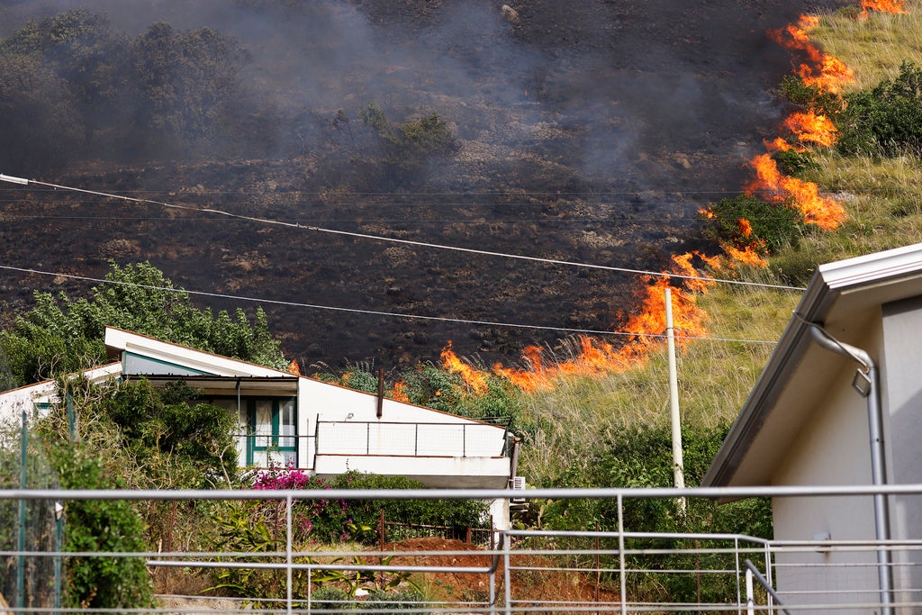 Flames burn behind houses in Capaci, near Palermo, in Sicily, southern Italy, Wednesday, July 26, 2023. On the island of Sicily, two people were found dead Tuesday in a home burned by a wildfire that temporarily shut down Palermo's international airport, according to Italian news reports. Regional officials said 55 fires were active on Sicily, amid temperatures in the 40s Celsius. (Alberto Lo Bianco/LaPresse via AP)