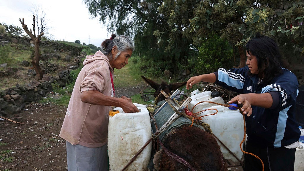 Emilia Segura, left, and her daughter Cecilia Rivera Segura arrange containers after filling them with water at a free, public well in Pueblo Santa Cruz Acalpixca, Xochimilco, on the outskirts of Mexico City, Saturday, Oct. 7, 2023. Segura, 62, has been selling water daily for over a decade with the help of her four donkeys. The system which provides the capital with over a quarter of its drinking water is 44% lower than it should be and have set a new record, according to government figures, and authorities have begun cutting water to the city. (AP Photo/Ginnette Riquelme)