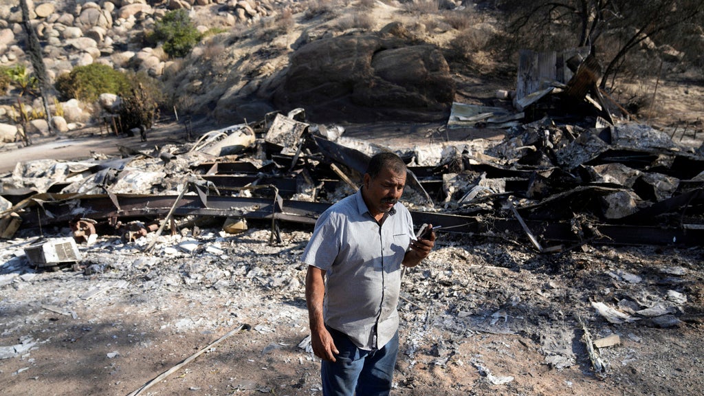 Luis Quinonez talks to a neighbor on the phone while surveying the damage to his property after the Highland Fire passed through Tuesday, Oct. 31, 2023, in Aguanga, Calif. (AP Photo/Marcio Jose Sanchez)