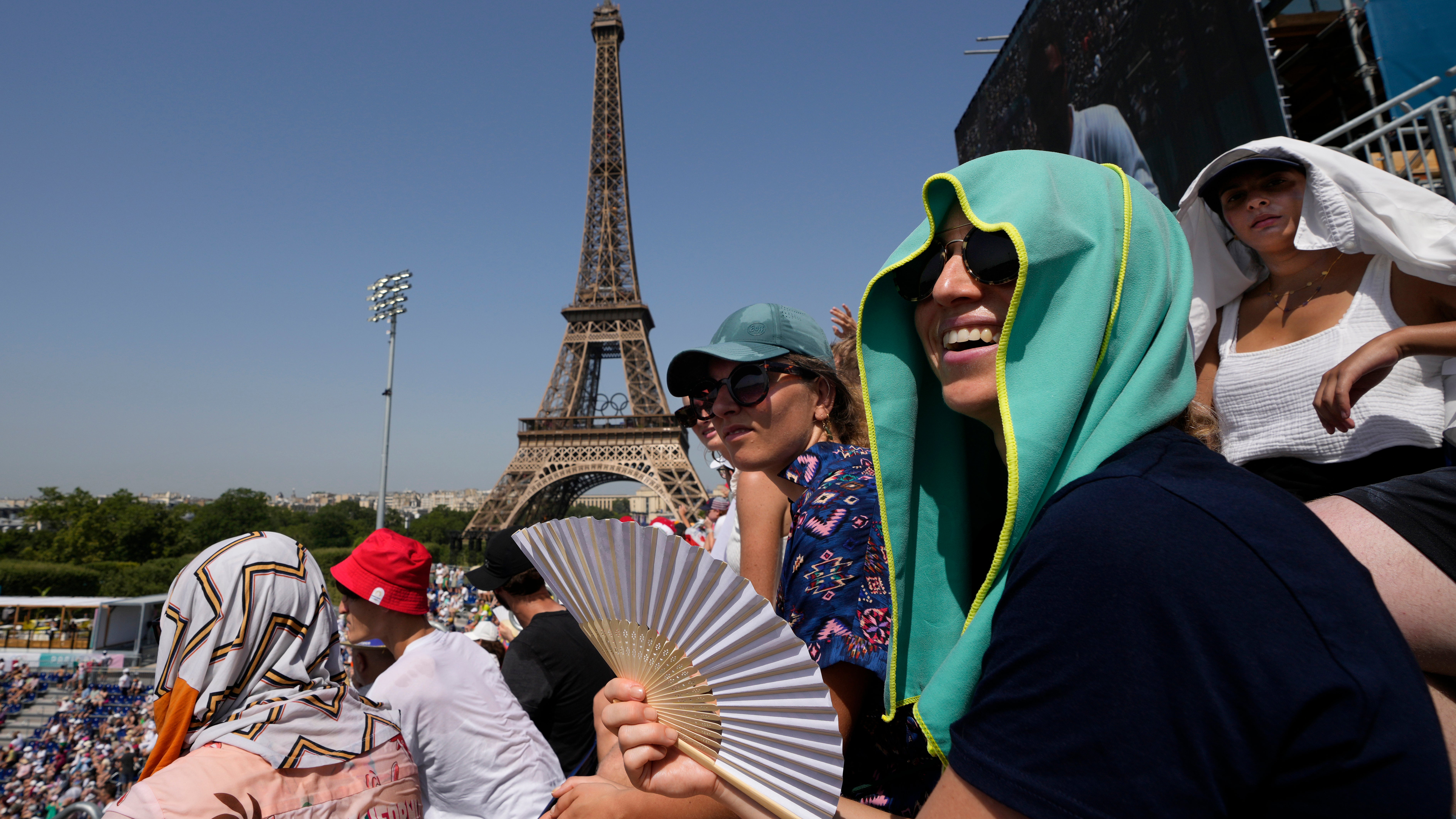 Stephanie Touissaint, foreground, uses a fan to keep cool in the sweltering heat at Eiffel Tower Stadium during a beach volleyball match between Cuba and Brazil at the 2024 Summer Olympics, Tuesday, July 30, 2024, in Paris, France. (AP Photo/Robert F. Bukaty)