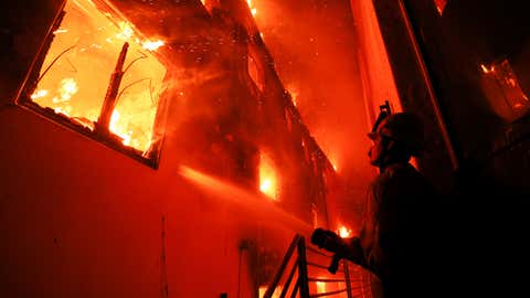 A firefighter works from a deck as the Palisades Fire burns a beachfront property Wednesday, Jan. 8, 2025, in Malibu, Calif. (AP Photo/Etienne Laurent)