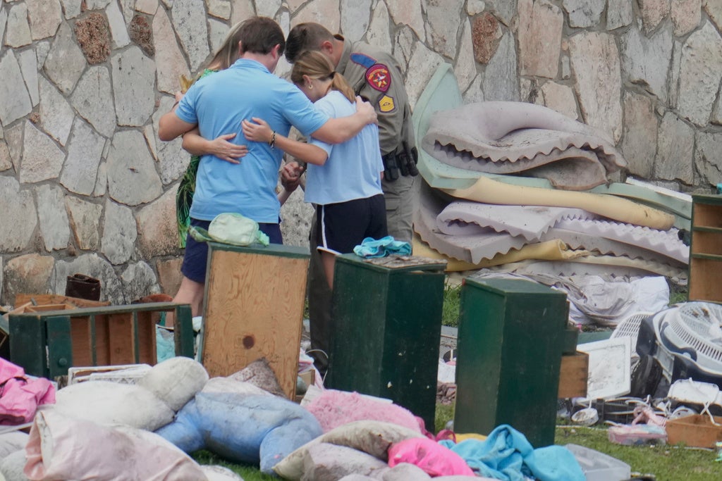 An officer prays with a family as they pick up items at Camp Mystic in Hunt, Texas on Wednesday, July 9, 2025. (AP Photo/Ashley Landis)