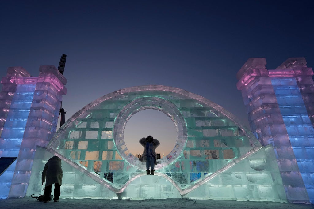 A visitors poses for photos near an ice sculpture before the opening ceremony for the annual Ice and Snow Festival held in Harbin in China's Heilongjiang province on Monday, Jan. 5, 2026. (AP Photo/Ng Han Guan)