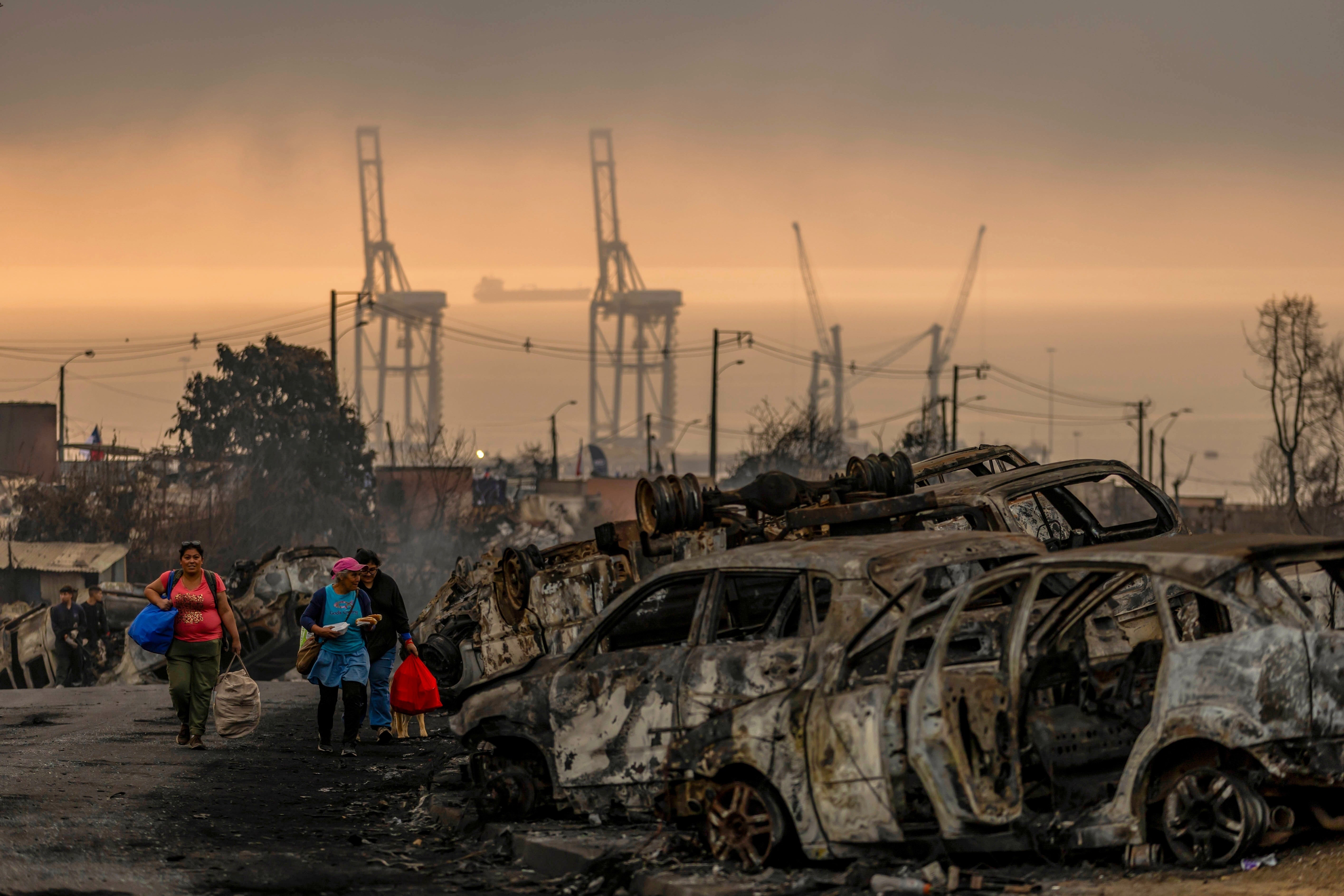 FILE - People transporting food to victims of wildfires walk past charred cars in Lirquen, Chile, Jan. 20, 2026. (AP Photo/Javier Torres, File)