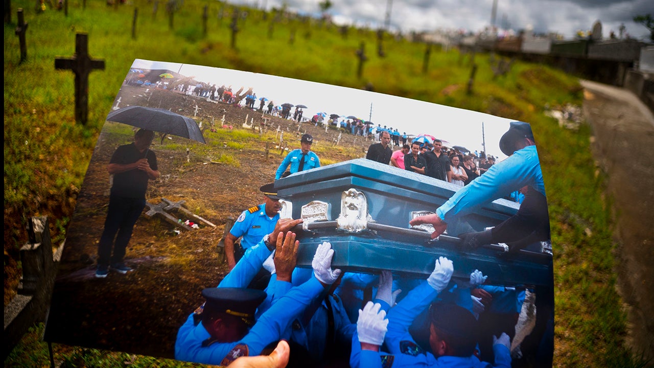 A printed photo taken on Sept. 29, 2017 showing police lifting the coffin of officer Luis Angel Gonzalez Lorenzo, who was killed during the passage of Hurricane Maria when he tried to cross a river in his car, is shown at the same cemetery in Aguada, Puerto Rico, May 31, 2018. The local police force of Aguadilla and Aguada lacks about a dozen officers since the storm, due to resignations and retirements. The U.S. territory's bankruptcy has frozen promotions, salaries, new hires and some police academies have even closed. (AP Photo/Ramon Espinosa)