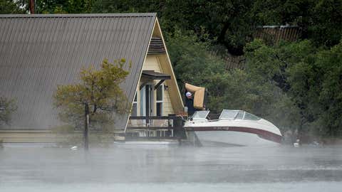 Loyd Reagan removes furniture from his house at Graveyard Point on Lake Travis on Wednesday, Oct. 17, 2018, in Austin, Texas. He used a boat to reach the second-floor deck of the house to save some of his belongings. (Jay Janner /Austin American-Statesman via AP)