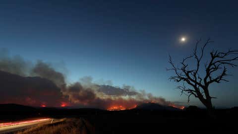 A car's taillights streak past at left as a wildfire threatening property glows at dusk near Clear Range, south of the Australian capital, Canberra, Friday, Jan. 31, 2020. The threat is posed by a blaze on Canberra's southern fringe that has razed more than 21,500 hectares (53,000 acres) since it was sparked by heat from a military helicopter landing light on Monday, the Emergency Services Agency said.(AP Photo/Rick Rycroft)