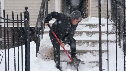 Skye DeJesus shovels her stairs while her dog Gordo pokes around in the snow in Jersey City, N.J., Monday, Feb. 1, 2021. A sprawling, lumbering winter storm is walloping the Eastern U.S., shutting down coronavirus vaccination sites, closing schools and halting transit. (AP Photo/Seth Wenig)