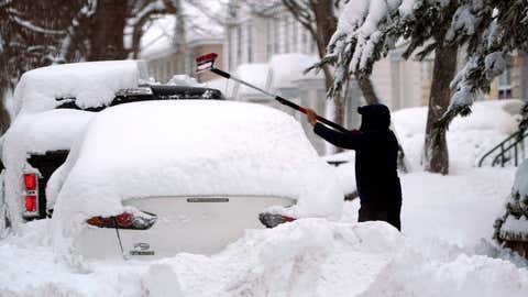 A man brushes snow off a car, Tuesday, Feb. 2, 2021, in Lawrence, Mass. A sprawling, lumbering winter storm has walloped the Eastern U.S., shutting down coronavirus vaccination sites, closing schools and halting transit. (AP Photo/Elise Amendola)