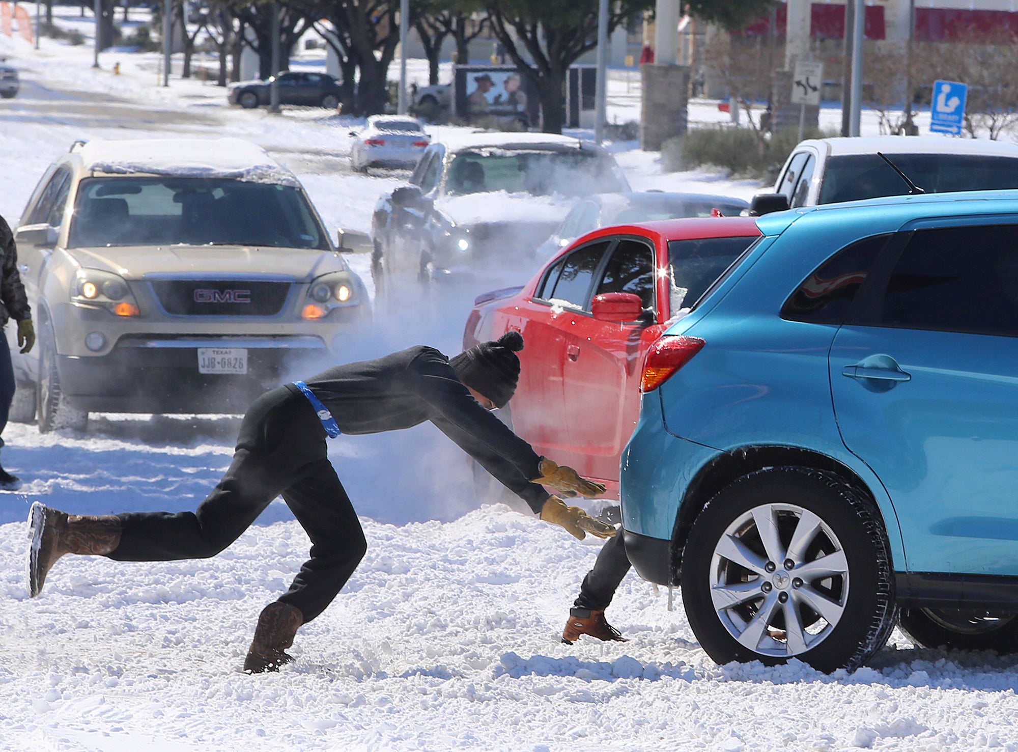 People push a car free after spinning out in the snow Monday, Feb. 15, 2021 in Waco, Texas.  A winter storm that brought snow, ice and plunging temperatures across the southern Plains and caused a power emergency in Texas stretched its frigid fingers down to the Gulf Coast.   (Jerry Larson/Waco Tribune-Herald via AP)