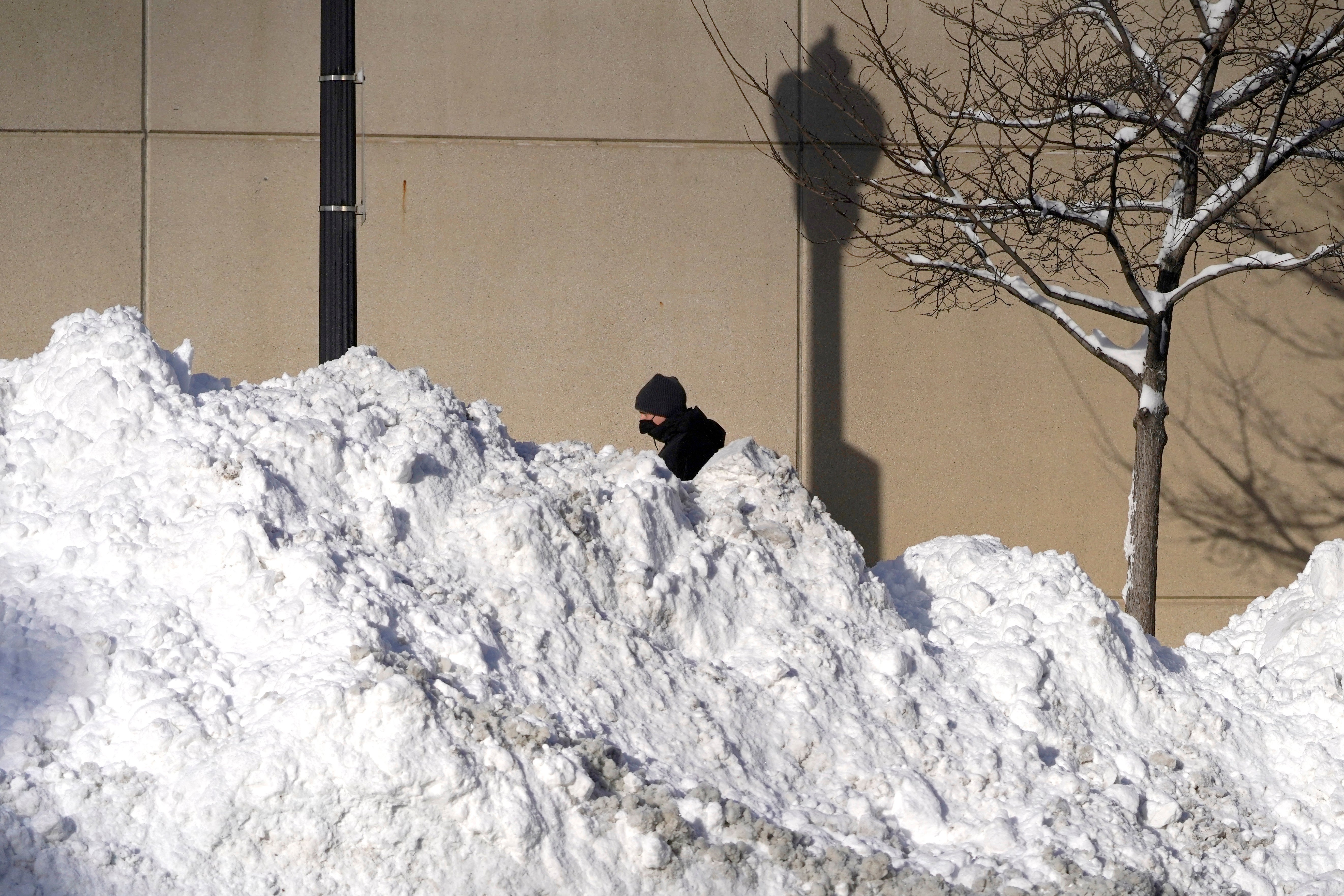 A man walks past mounds of plowed snow from nine consecutive days of measurable and fresh fallen snow Tuesday, Feb. 16, 2021, in Chicago. (AP Photo/Charles Rex Arbogast)
